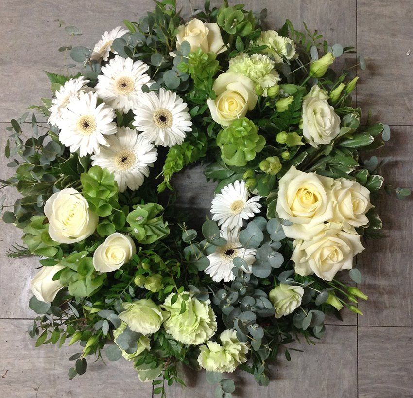 Floral wreath with white and green flowers, on a gray tile surface.