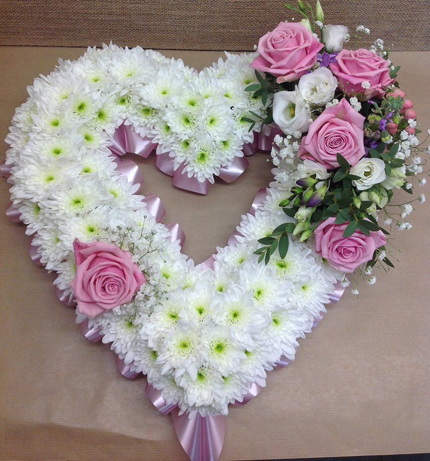 Floral heart arrangement, white chrysanthemums with pink roses and accents, resting on a surface.