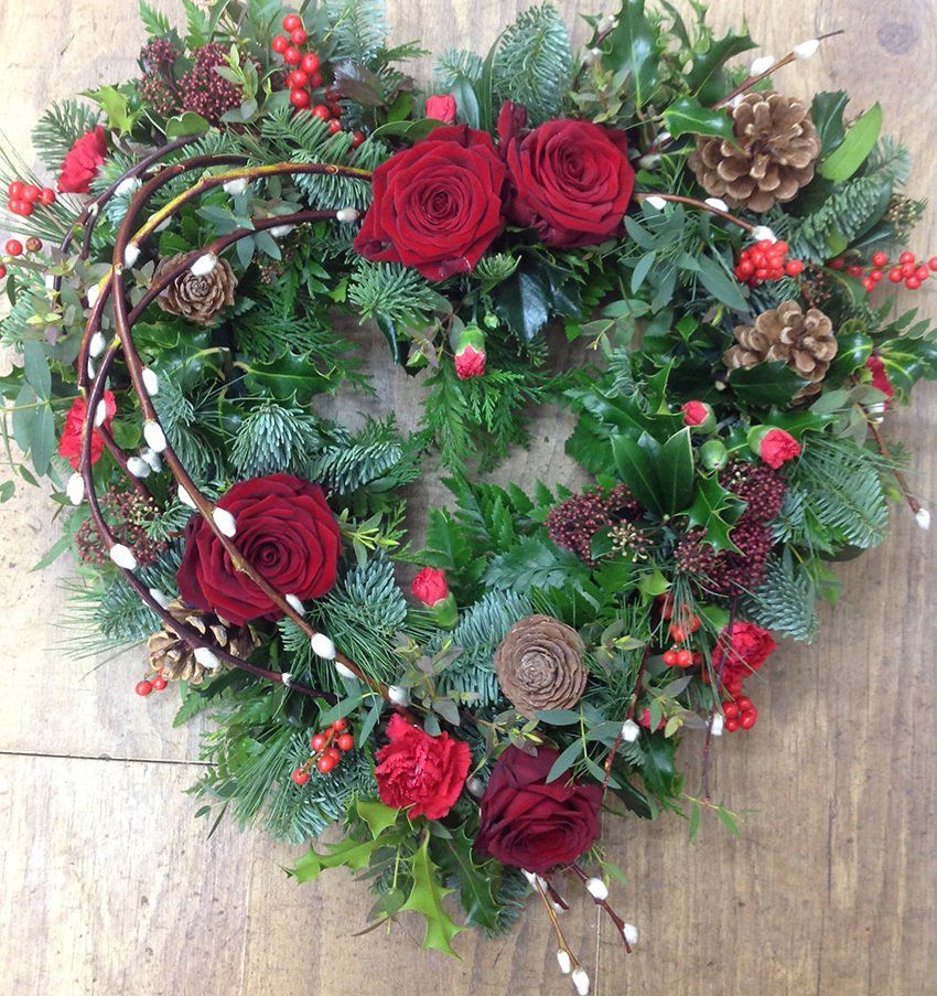 Heart-shaped wreath with red roses, berries, pine cones, and green foliage.