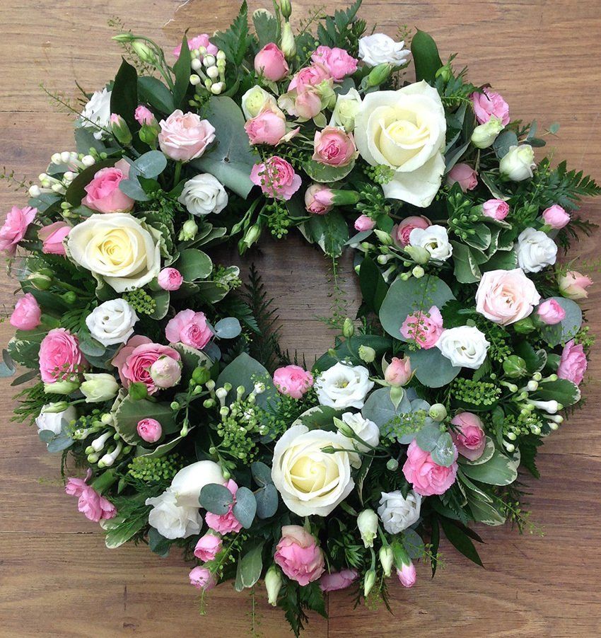 Wreath of white and pink roses, greenery, set on a wooden surface.