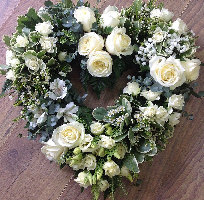 Heart-shaped floral arrangement with white roses and greenery on a wooden surface.