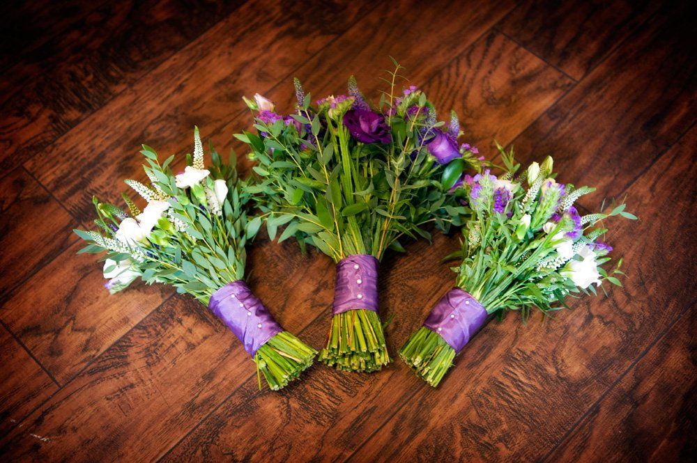Three flower bouquets tied with purple ribbon on a wooden surface.