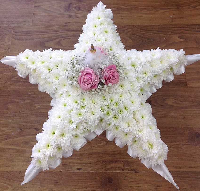 Floral star-shaped arrangement with white chrysanthemums, pink roses, and baby's breath on wooden floor.