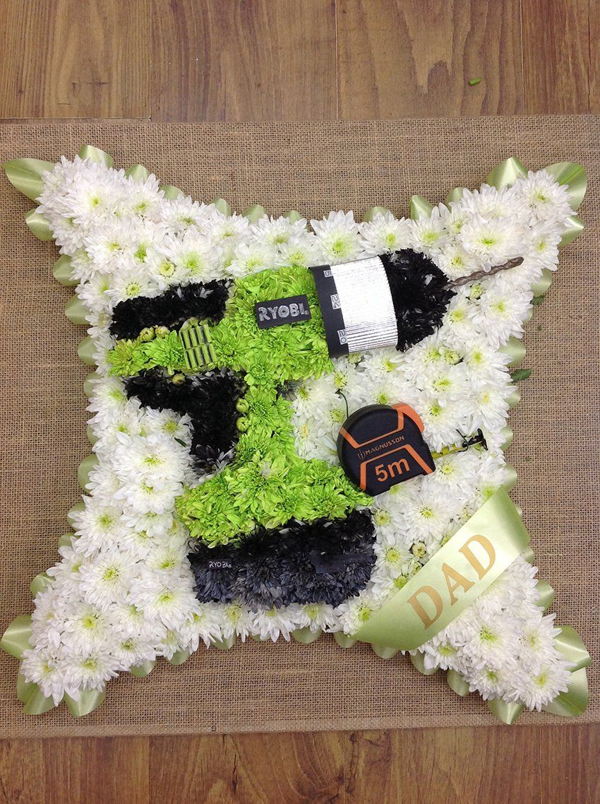 Floral tribute shaped like a drill, tape measure, and 