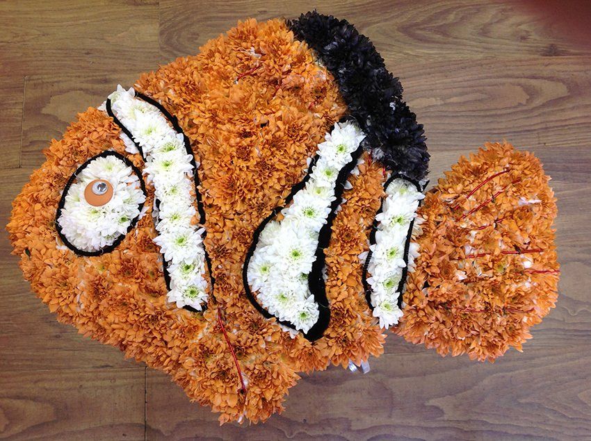 Floral arrangement shaped like an orange clownfish with white stripes and black accents on a wooden surface.