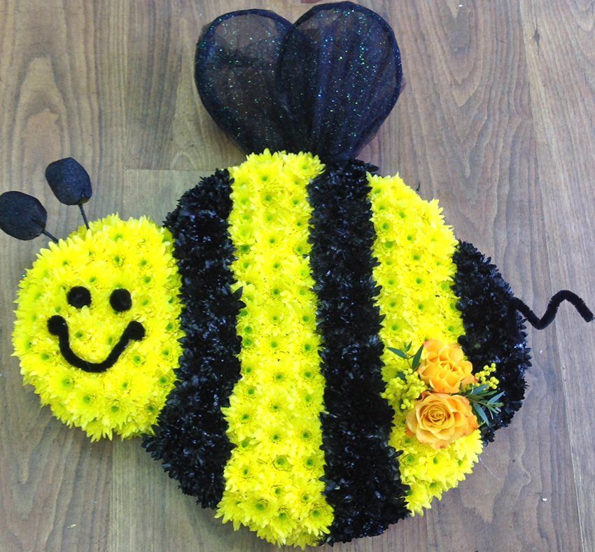 Floral arrangement of a bumblebee; yellow and black flowers with a smiling face and orange flowers.