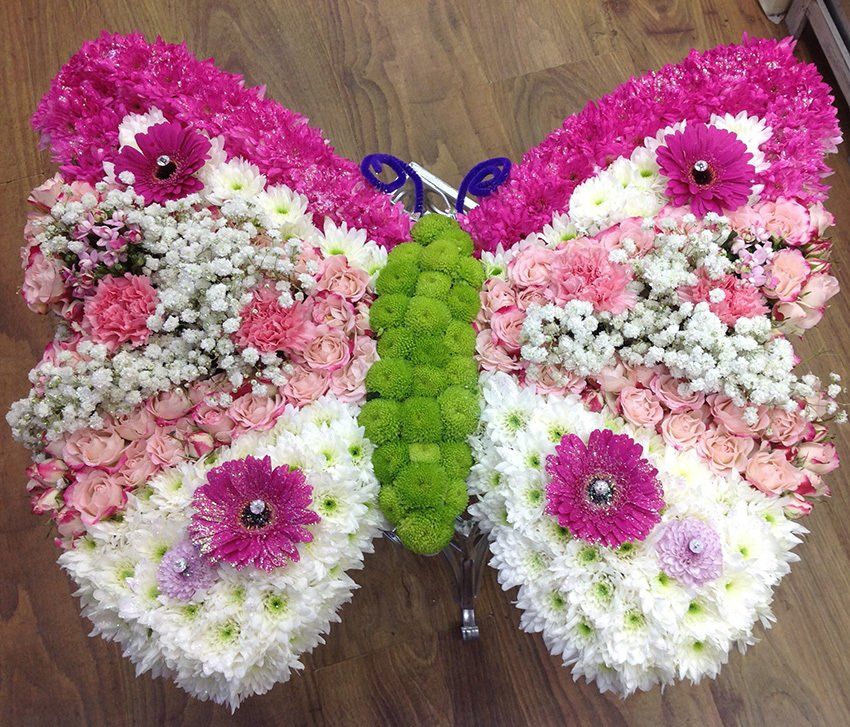 Butterfly-shaped floral arrangement; pink, white, and green flowers on a wooden surface.