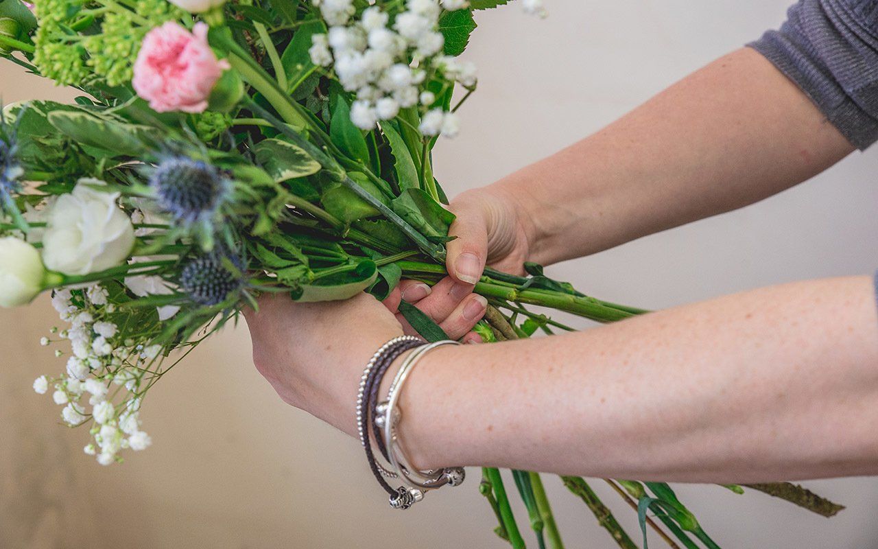 Person's hands tying a bouquet of colorful flowers with greenery.