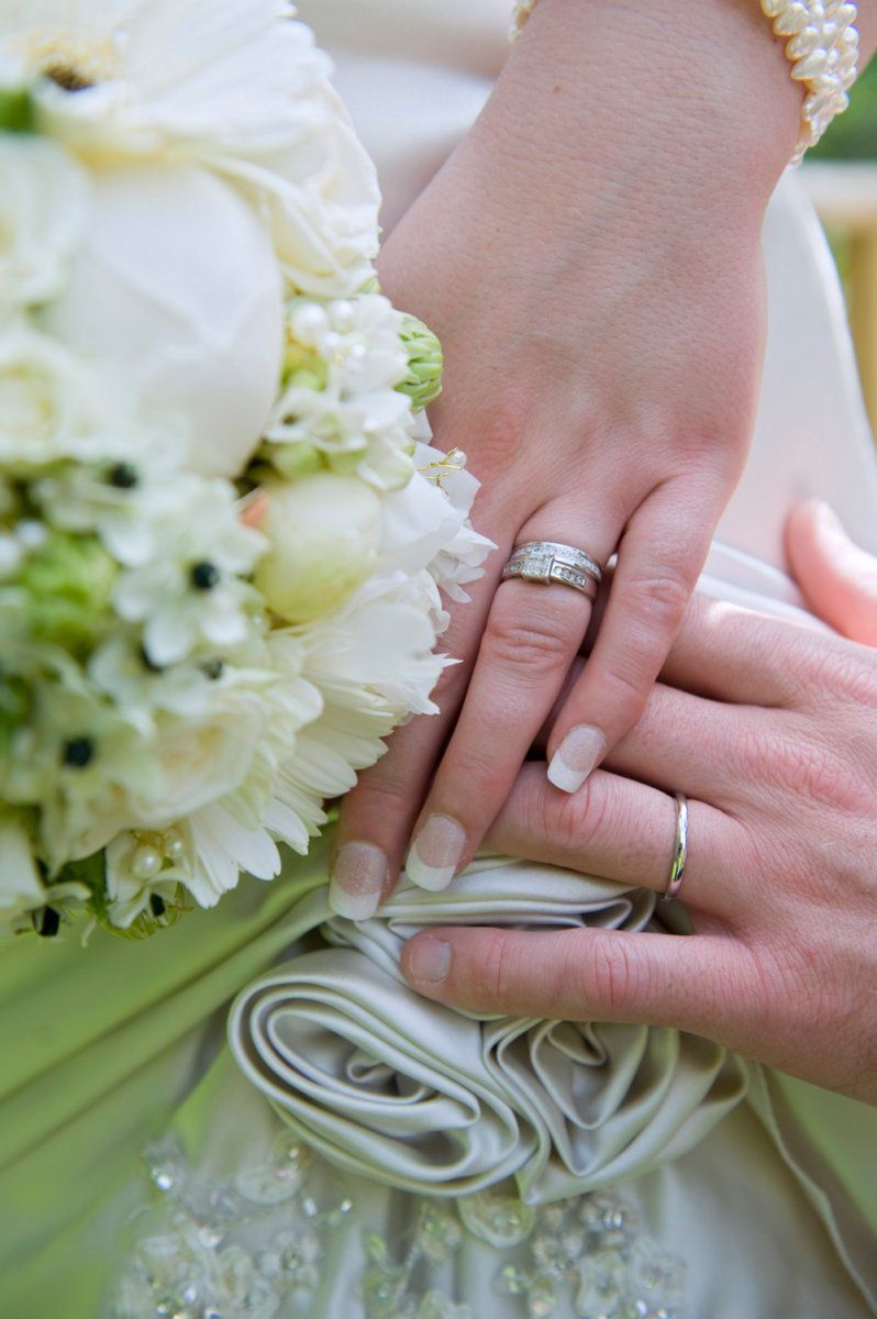 Hands with wedding rings on a white dress, holding a bouquet of white flowers.