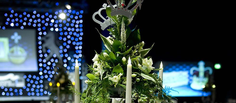 Arrangement of white flowers and candles.  Crowns are at the top, and there is a blue backdrop.