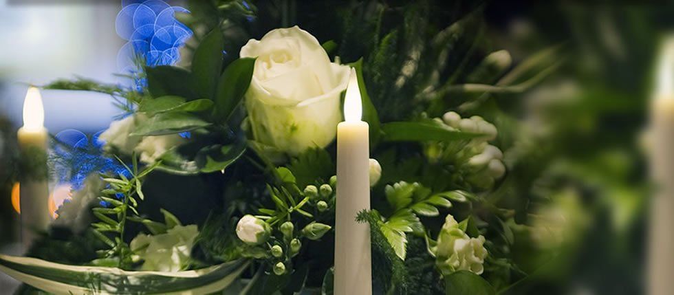 Candle amidst white roses and greenery. Soft lighting.