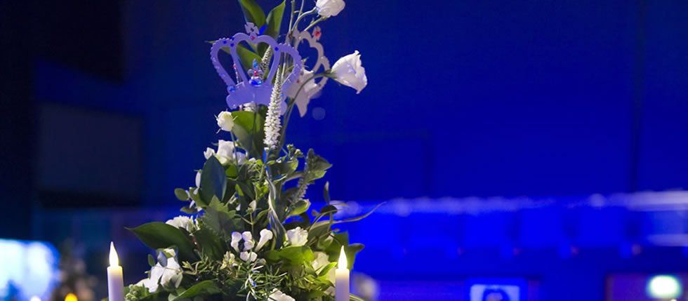 White floral arrangement with a crown decoration, candles, and a blue background.