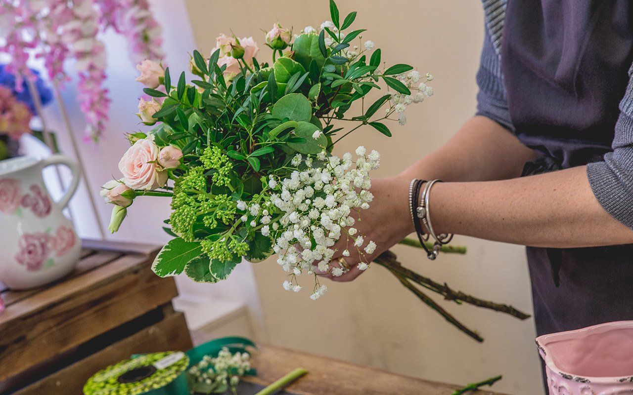 Florist arranging a bouquet with pink roses, baby's breath, and greenery. Close-up view with hands visible.