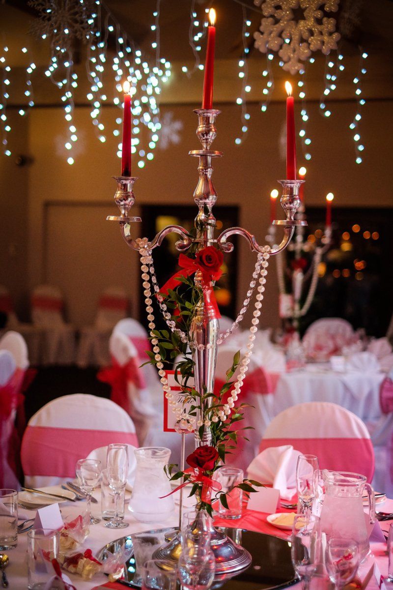 Candlelit reception table with candelabra, pearls, and red accents. Chairs have pink sashes.