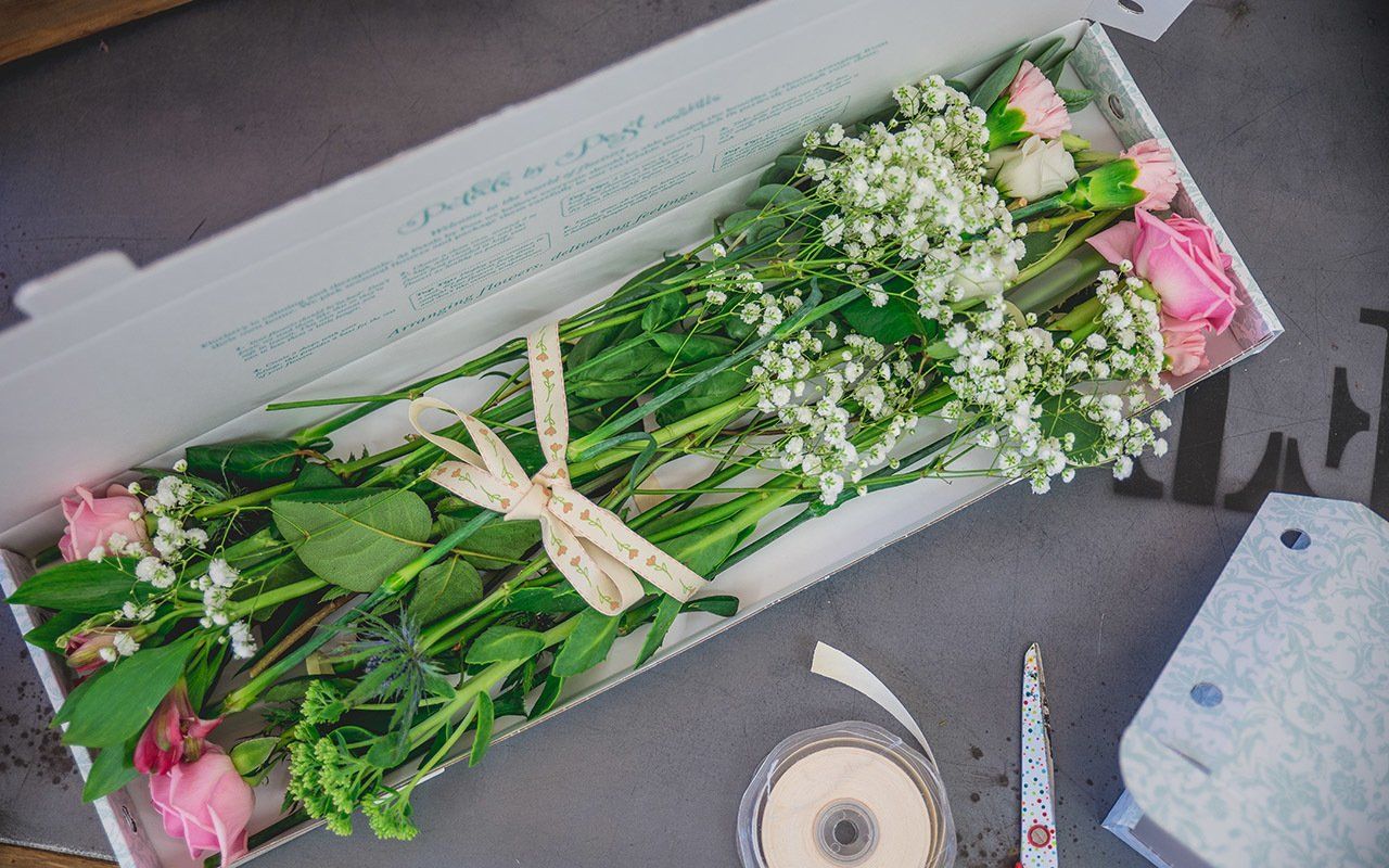 Pink roses and baby's breath arranged in a white box, tied with ribbon.