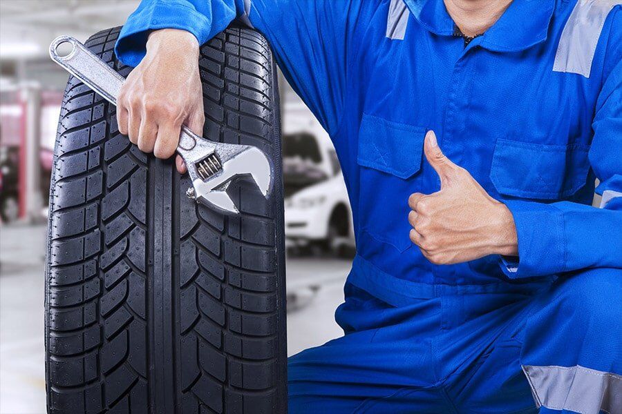 A mechanic is holding a tire and a wrench and giving a thumbs up.