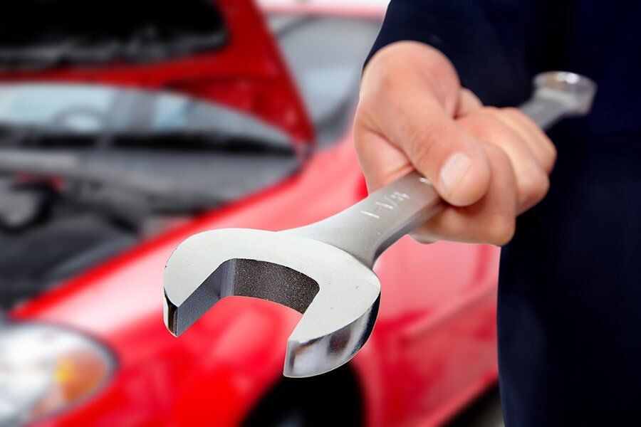 A person is holding a wrench in front of a red car