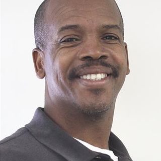 Smiling Black man with short hair and a mustache in front of a white background.