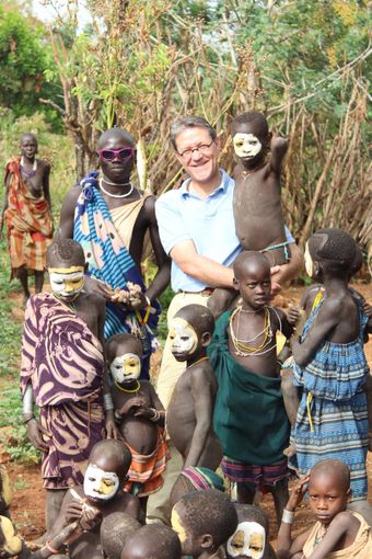 Woman standing with a group of smiling children in colorful clothing outdoors among greenery