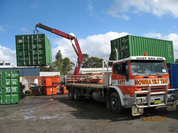 flat bed truck picking up green container with crane
