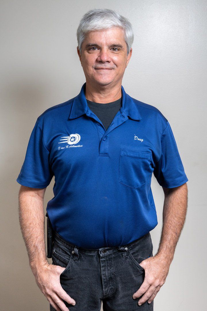 Man standing against a plain wall, wearing a blue polo shirt and dark jeans, with hands in pockets.