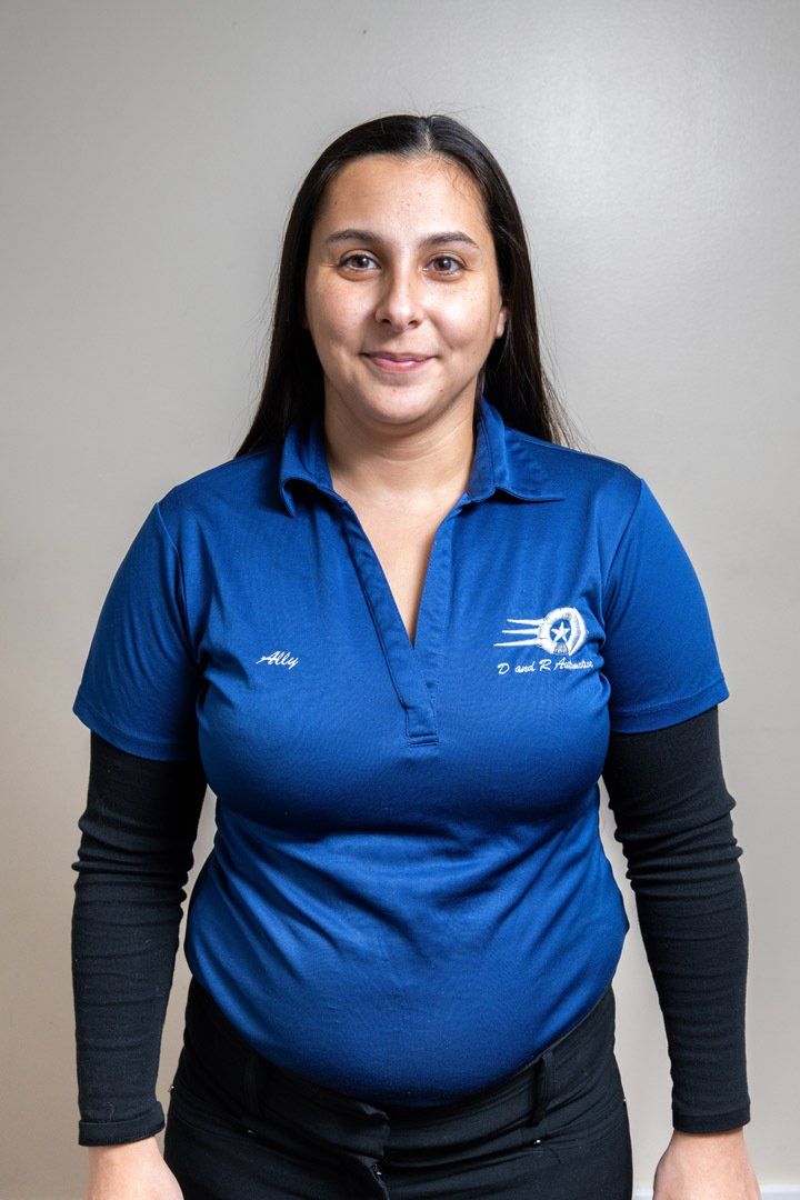 Woman standing against a gray wall, wearing a blue polo shirt and black sleeves, facing the camera.