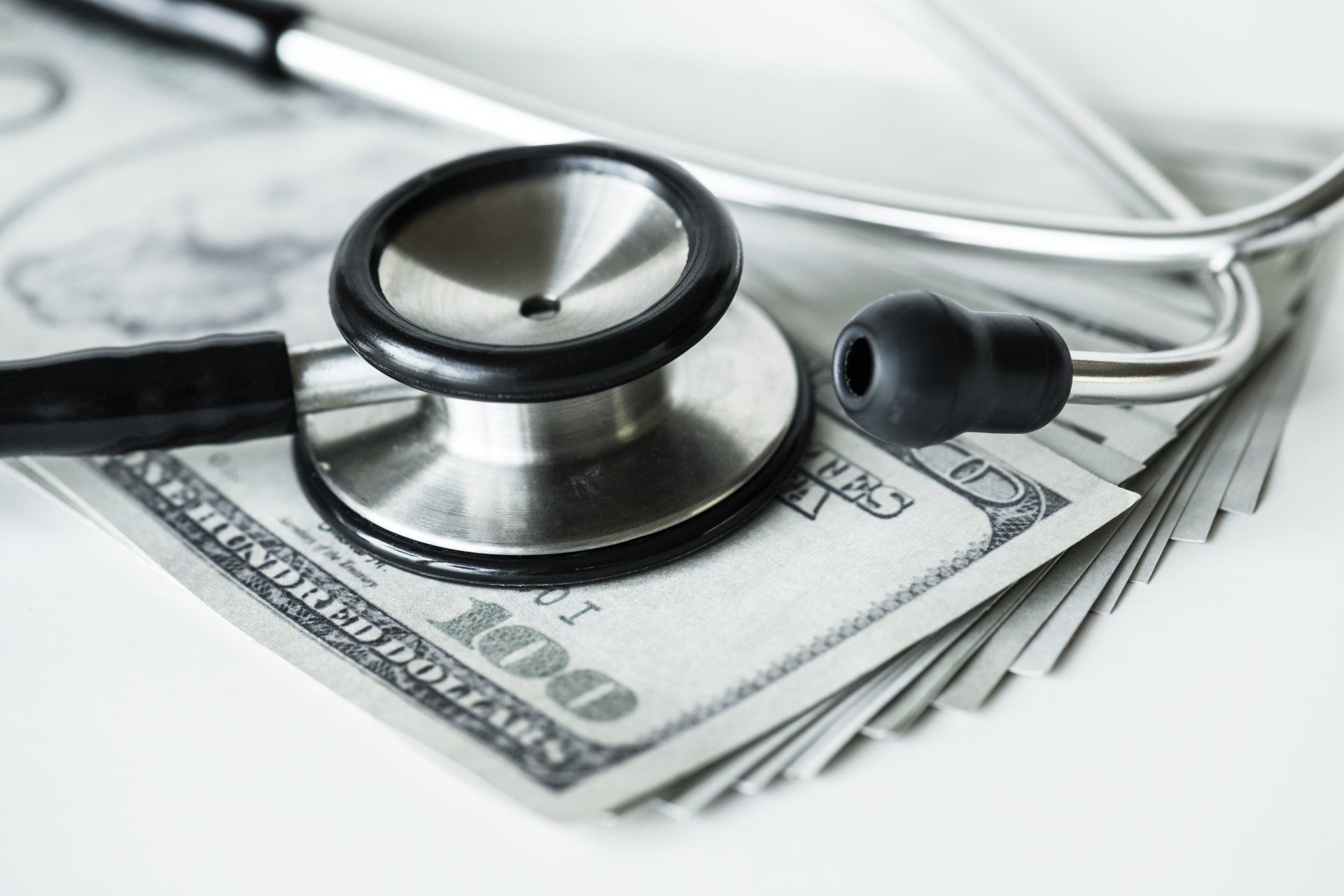 A stethoscope  and 100 dollar bills underneath on a table