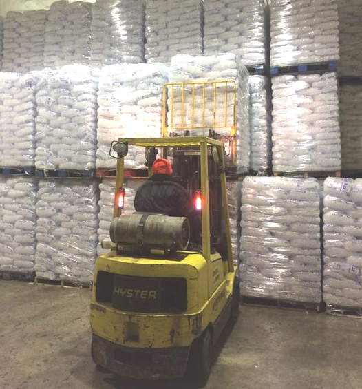 Yellow forklift in a warehouse stacked with wrapped pallets, viewed from behind.