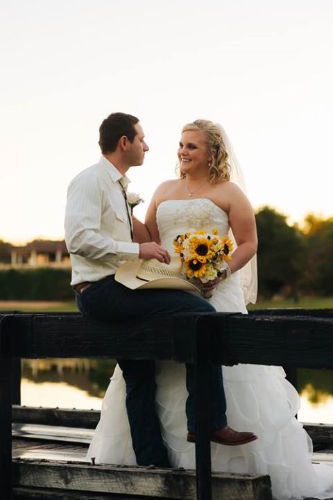 A bride and groom are sitting on a bridge looking at each other.