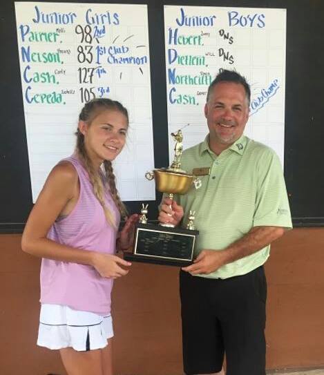 A man and a girl holding a trophy in front of a board that says junior girls and junior boys