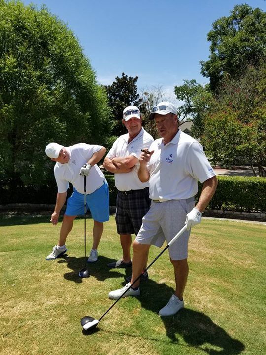 Three men are standing on a golf course holding golf clubs