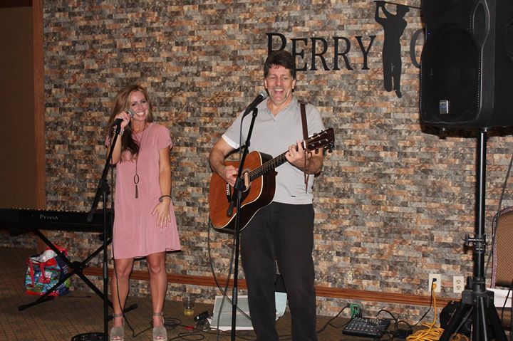 A man is playing a guitar and a woman is singing into a microphone.