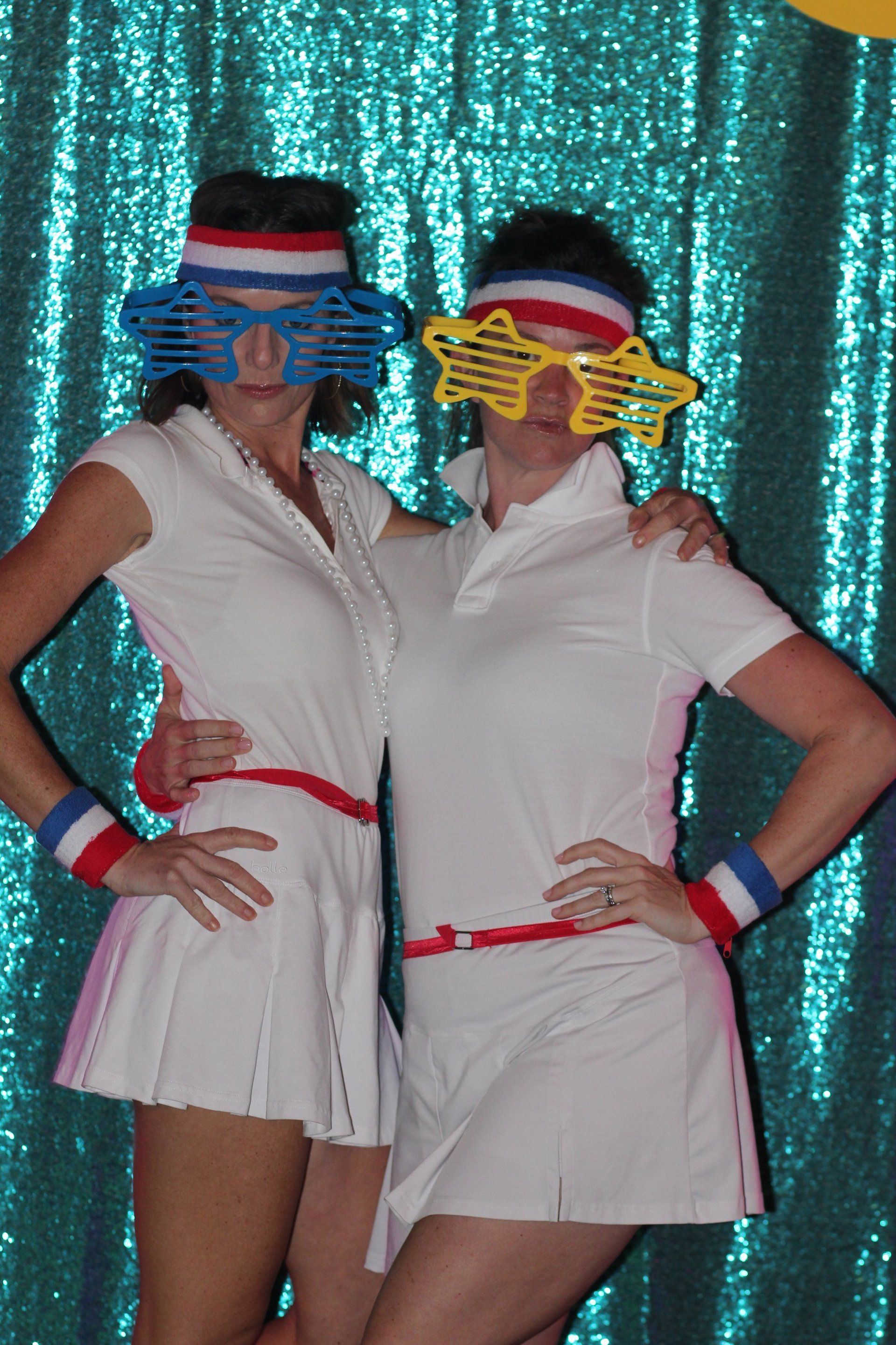 Two women wearing tennis outfits and sunglasses pose for a picture