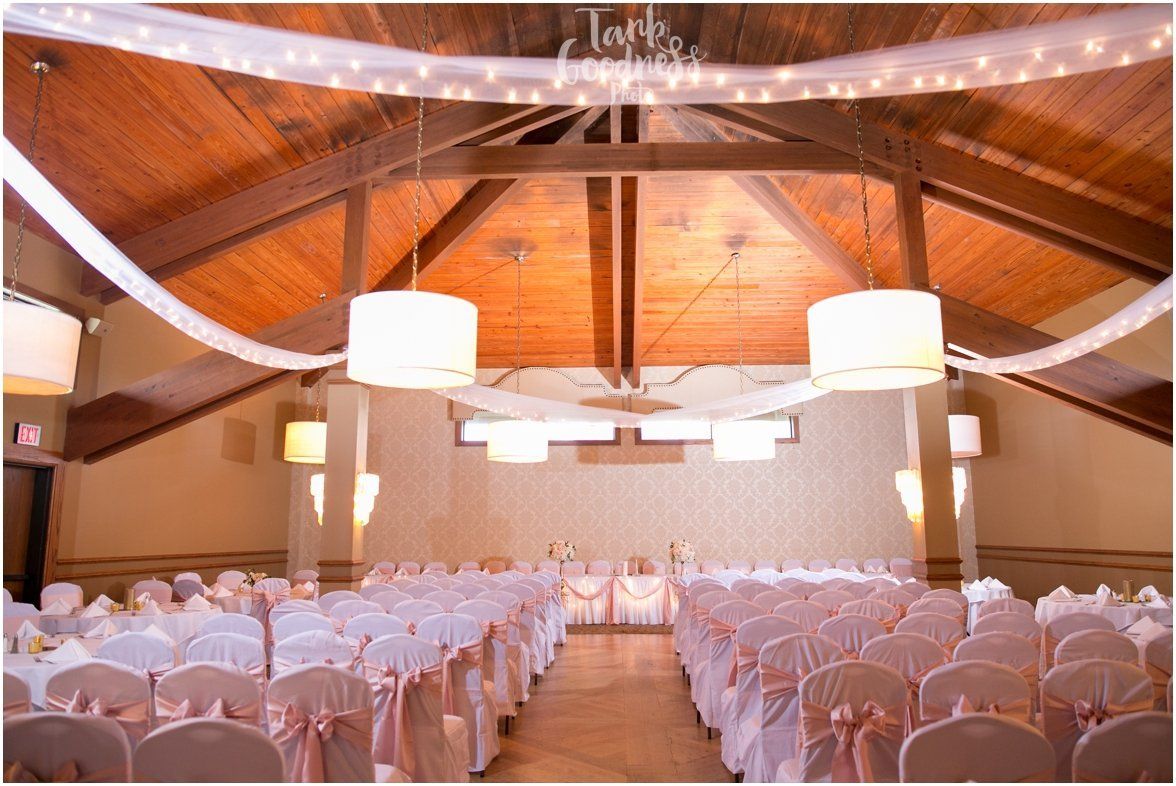 A wedding ceremony is taking place in a large room with lots of chairs and lights hanging from the ceiling.