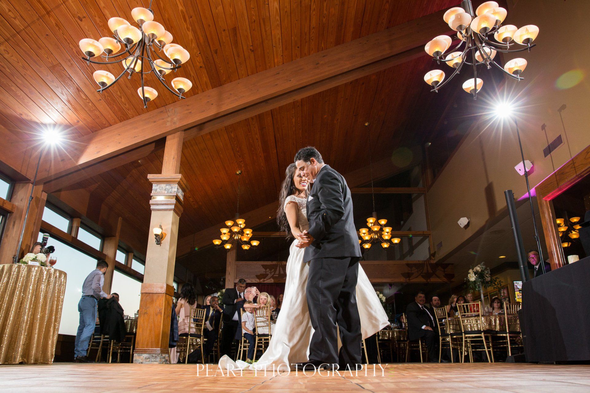 A bride and groom are dancing in a large room at their wedding reception.