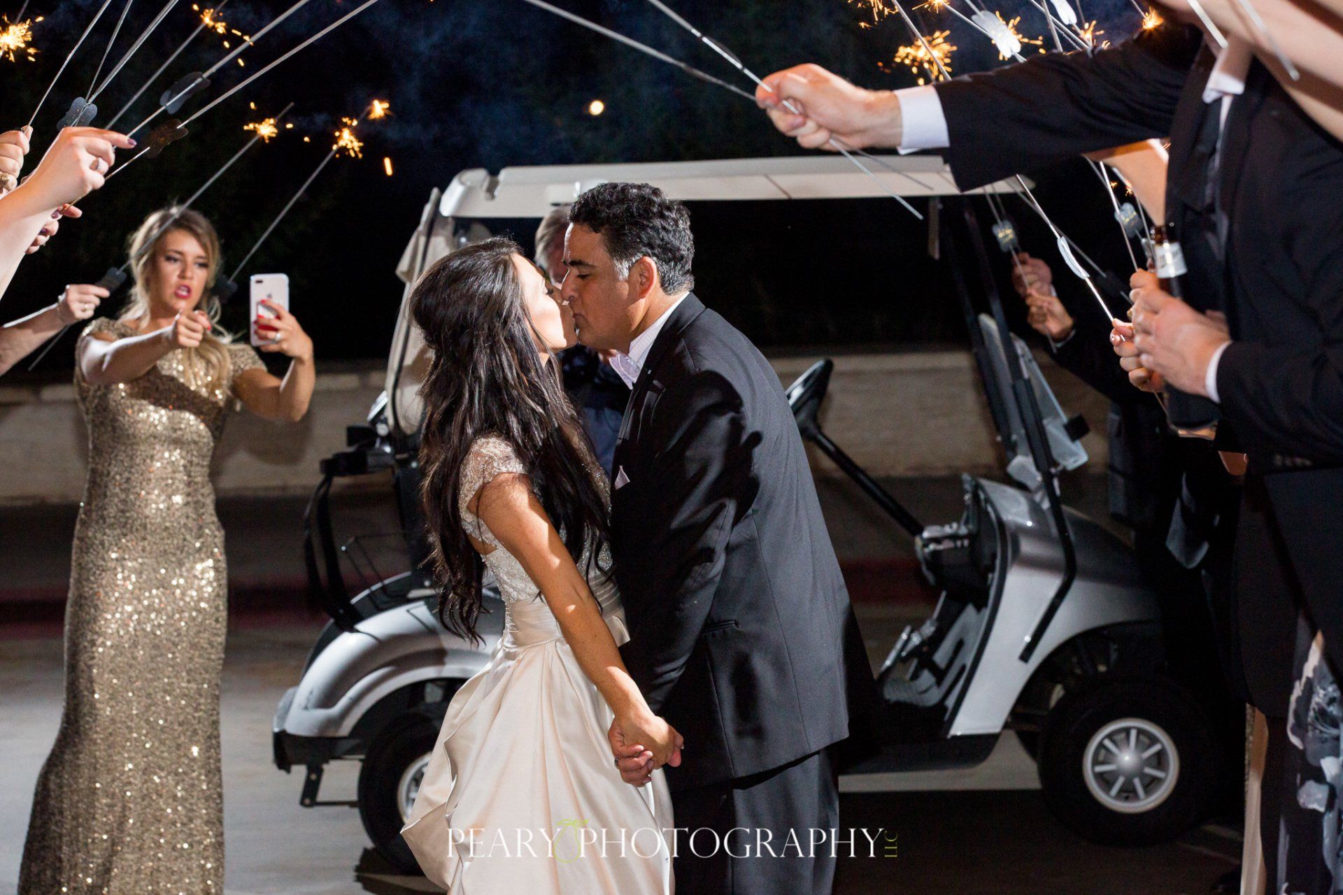 A bride and groom kissing in front of a golf cart with sparklers.