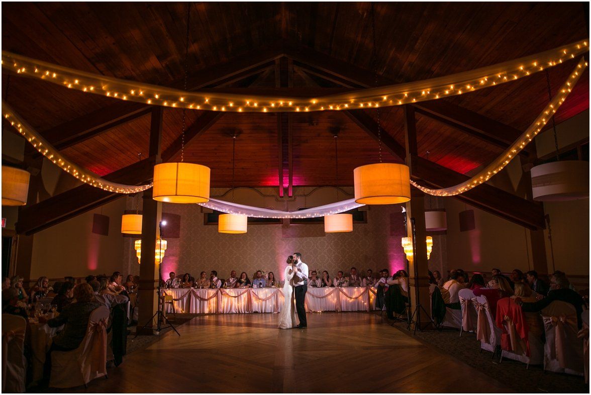 A bride and groom are dancing in a large room at their wedding reception.
