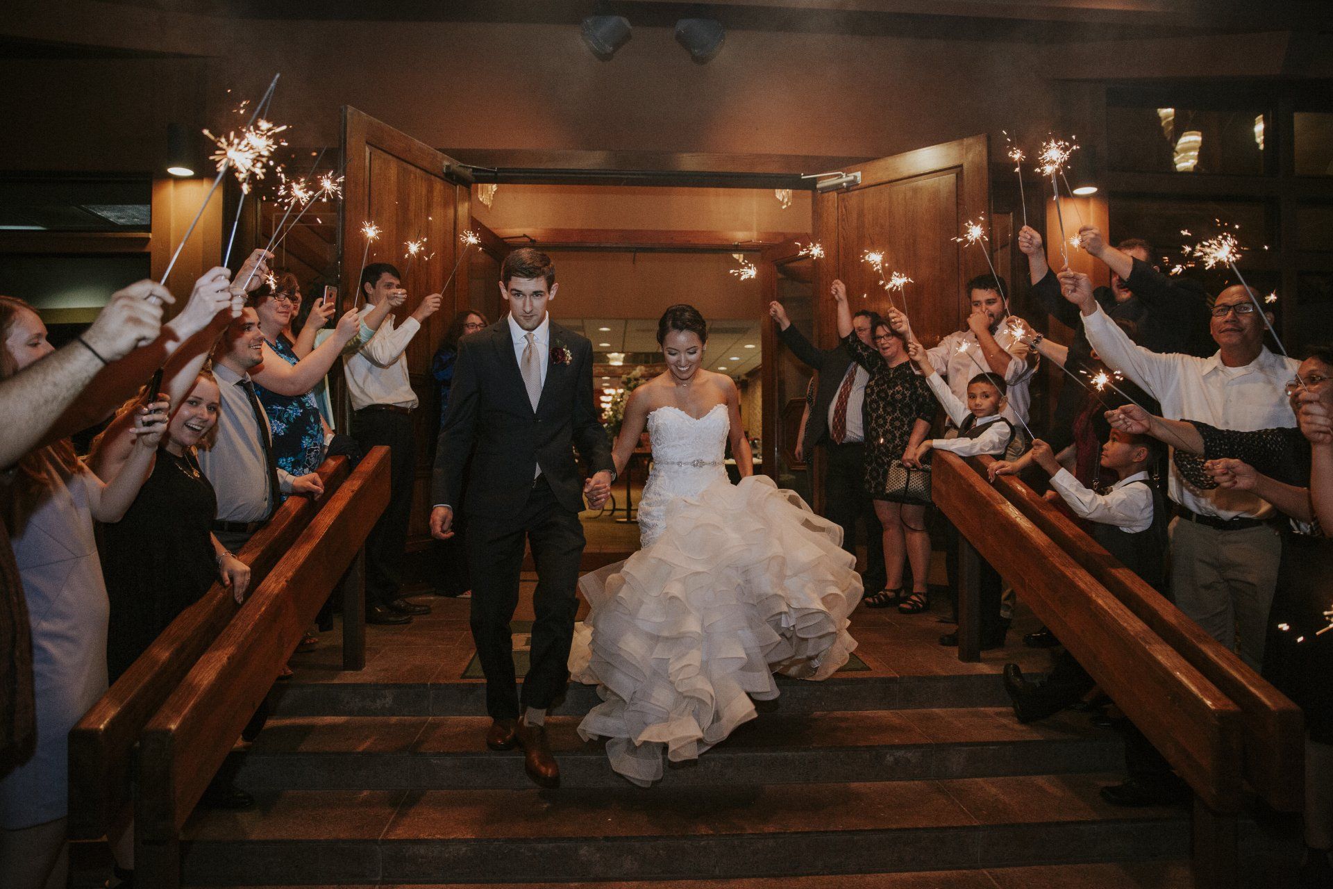 A bride and groom are walking down the stairs while holding sparklers.