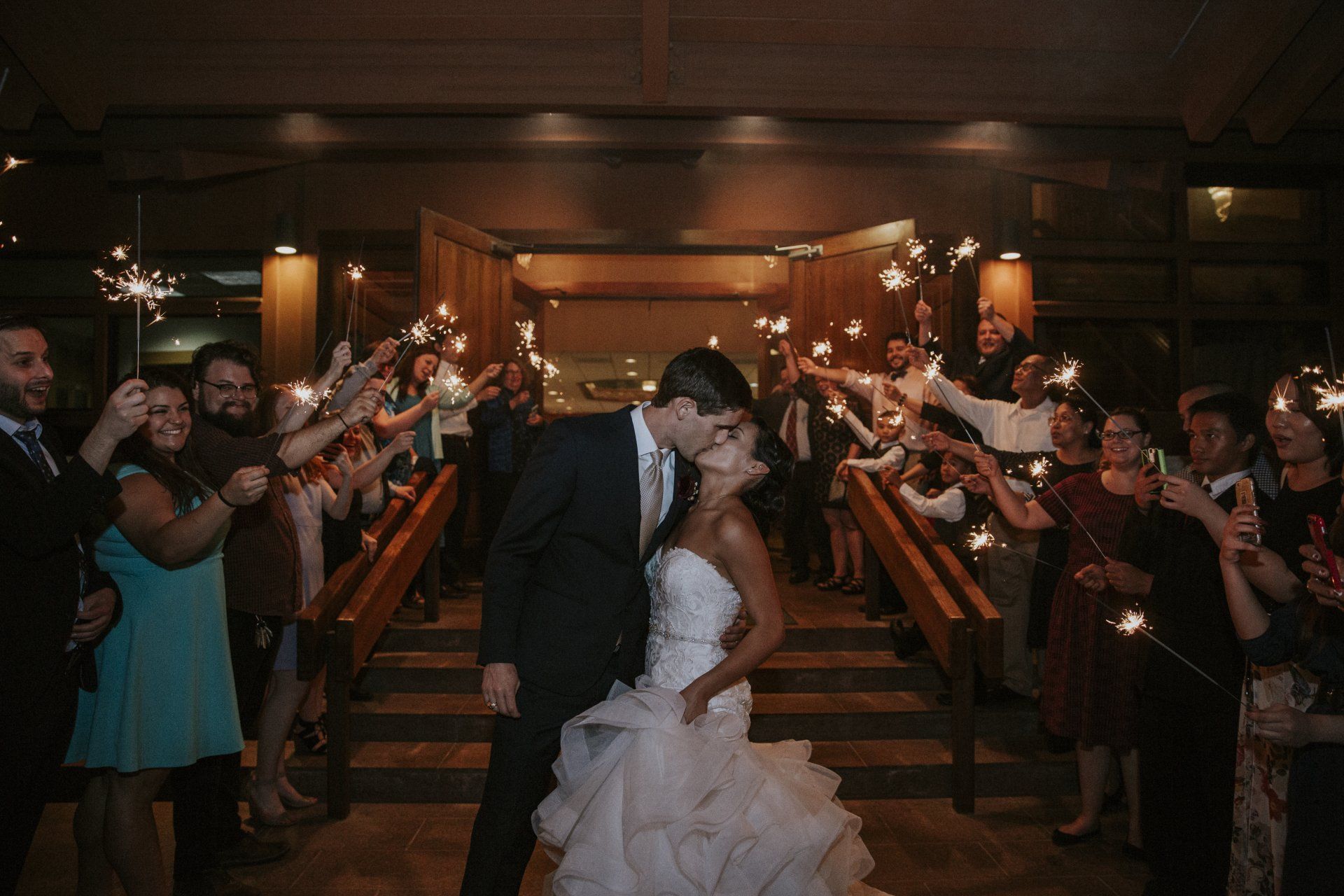 A bride and groom kissing in front of a crowd of people holding sparklers.