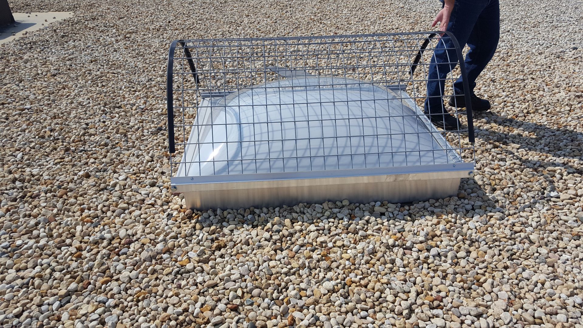A person is standing next to a metal structure on a gravel ground.