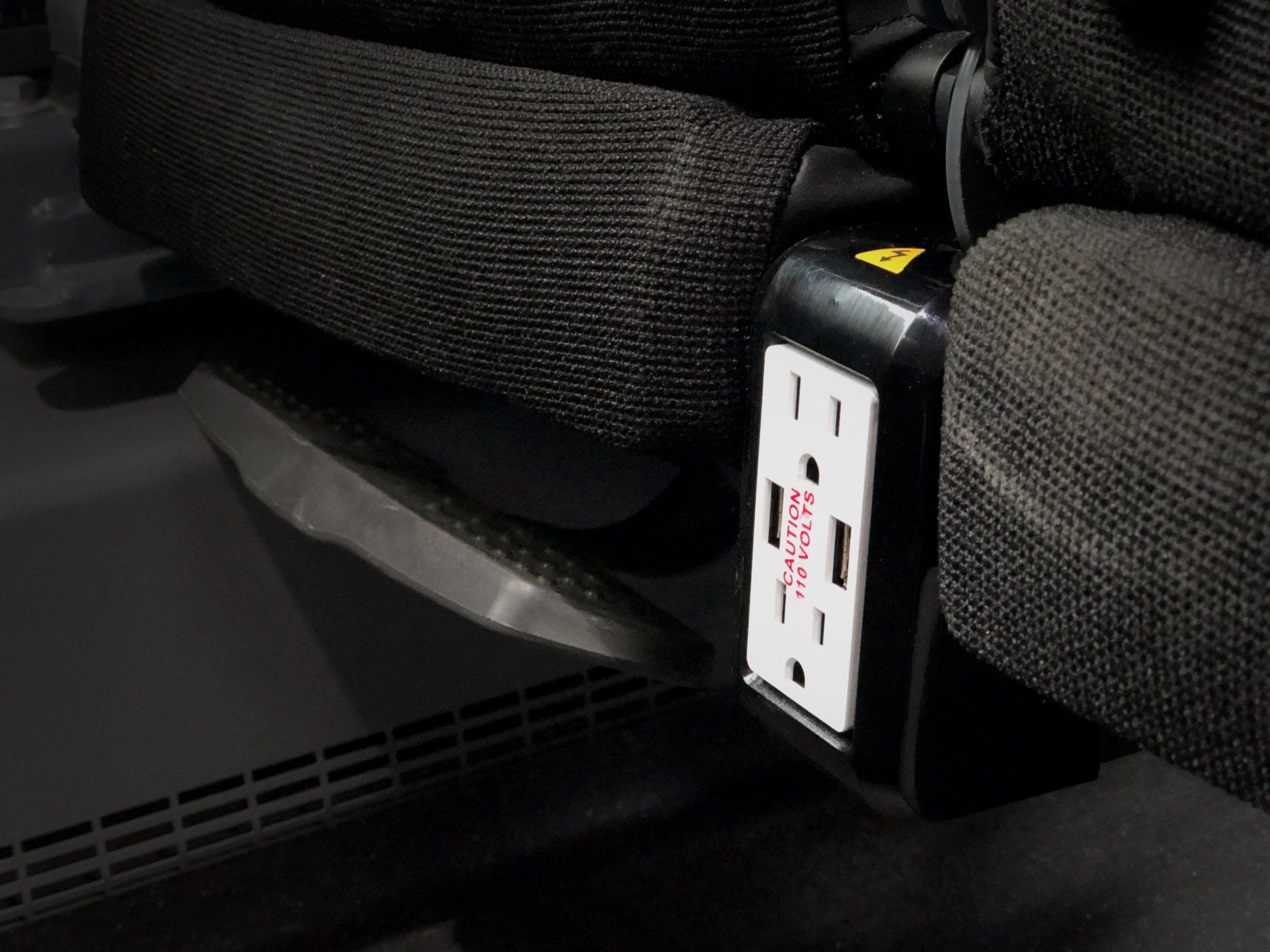 A power outlet is attached to the side of a seat.