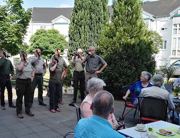 Menschen in Uniform halten Instrumente vor sitzenden älteren Menschen, Außenterrasse.
