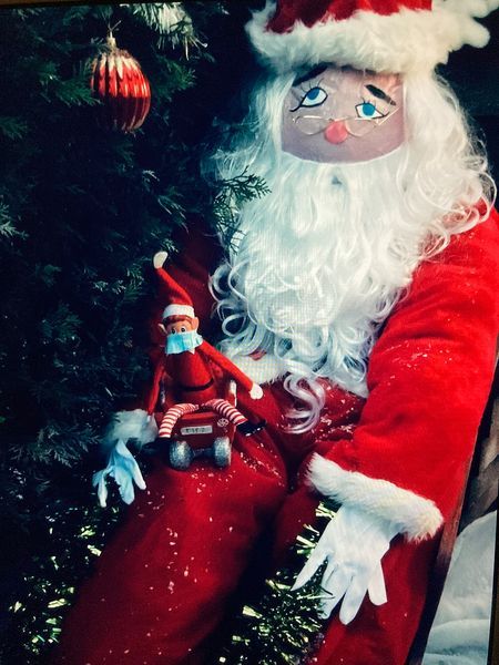 Santa in red suit holding a small red doll by a Christmas tree