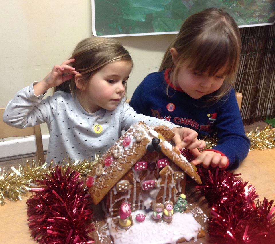 Two children decorating a gingerbread house with pink and gold tinsel