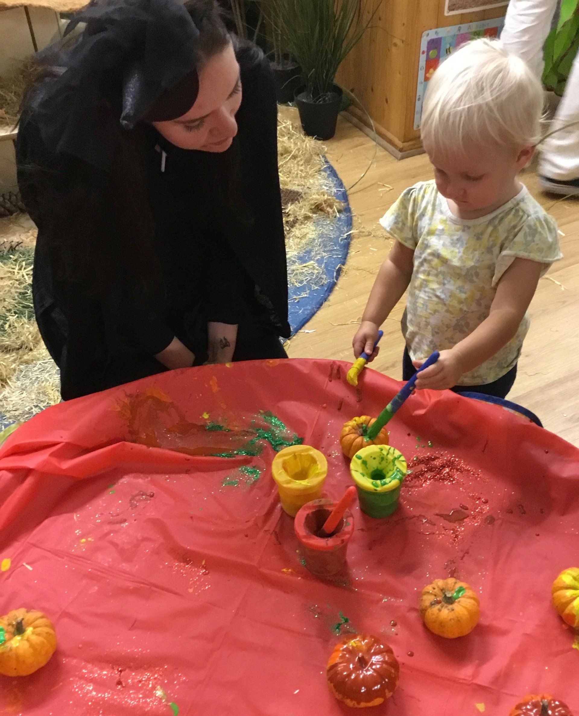 Adult and child painting on a red tablecloth with bright cups and pumpkins in a craft activity