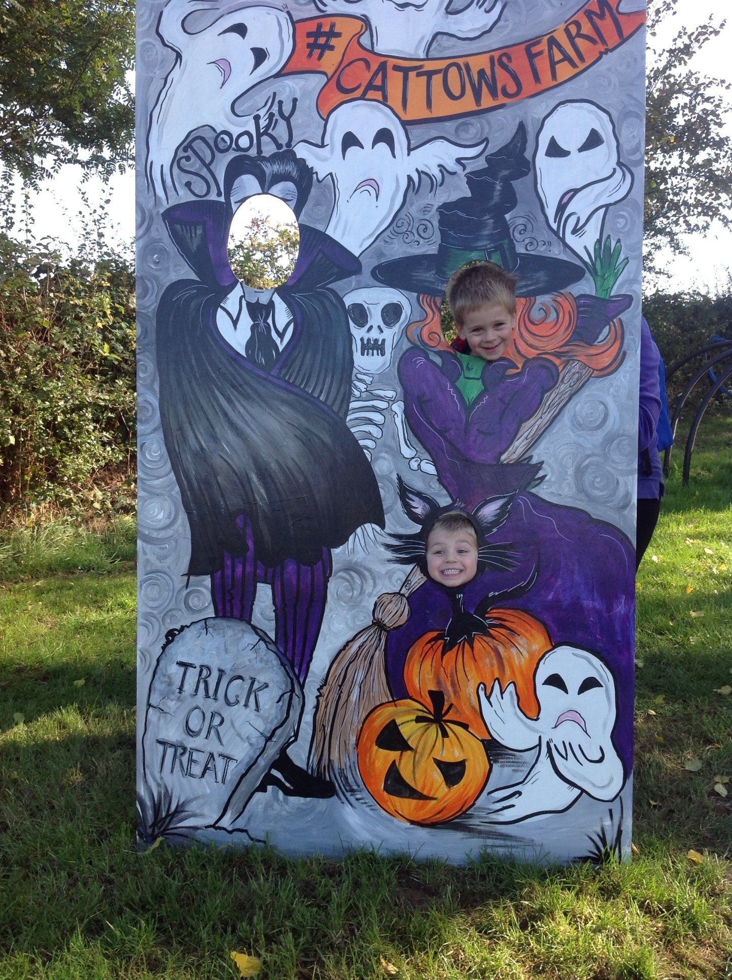 Halloween cutout board with ghosts, pumpkins, and children posing in costume holes outside Cattow’s Farm