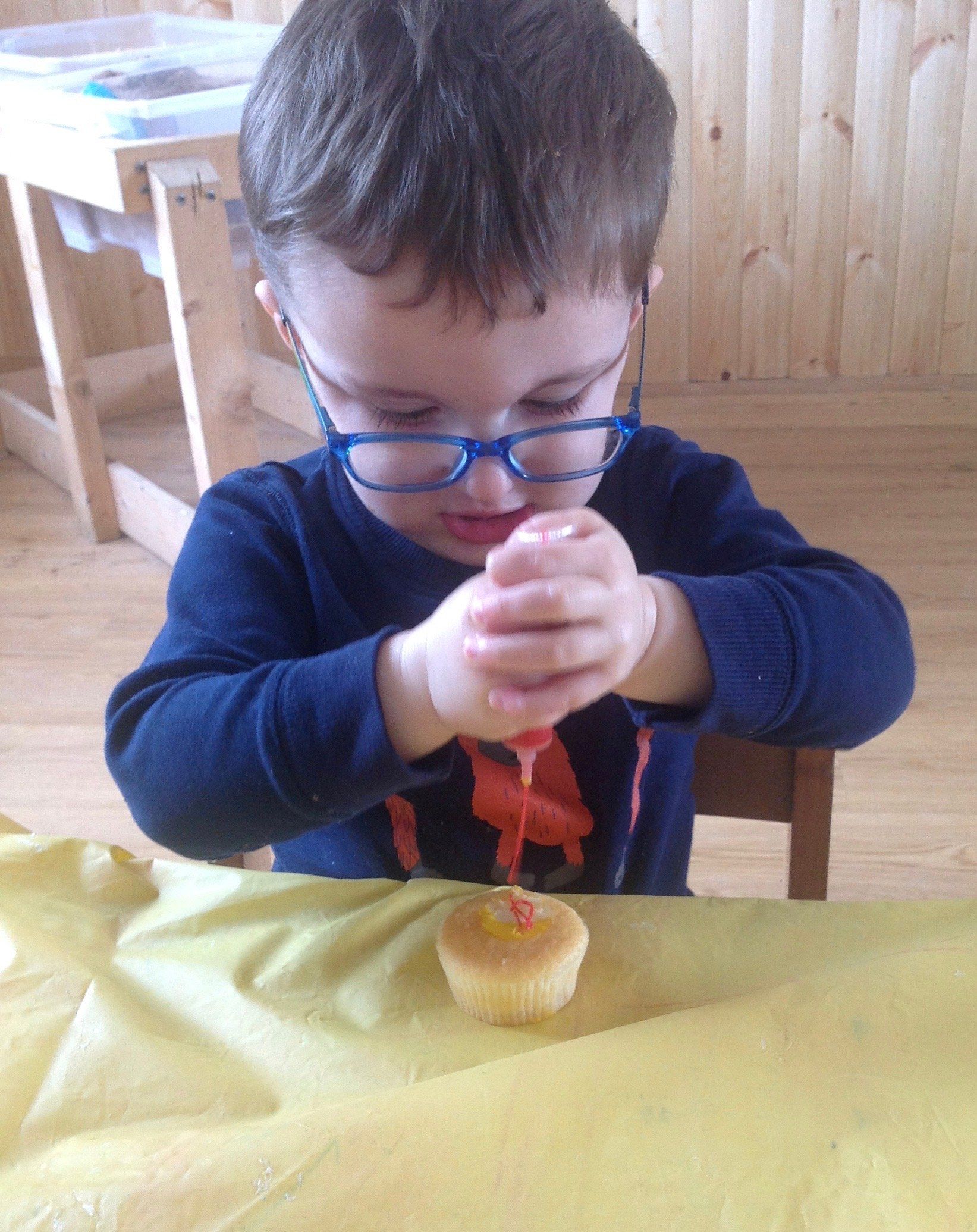 Child in blue sweater concentrating while squeezing a small object at a table with a yellow cloth.
