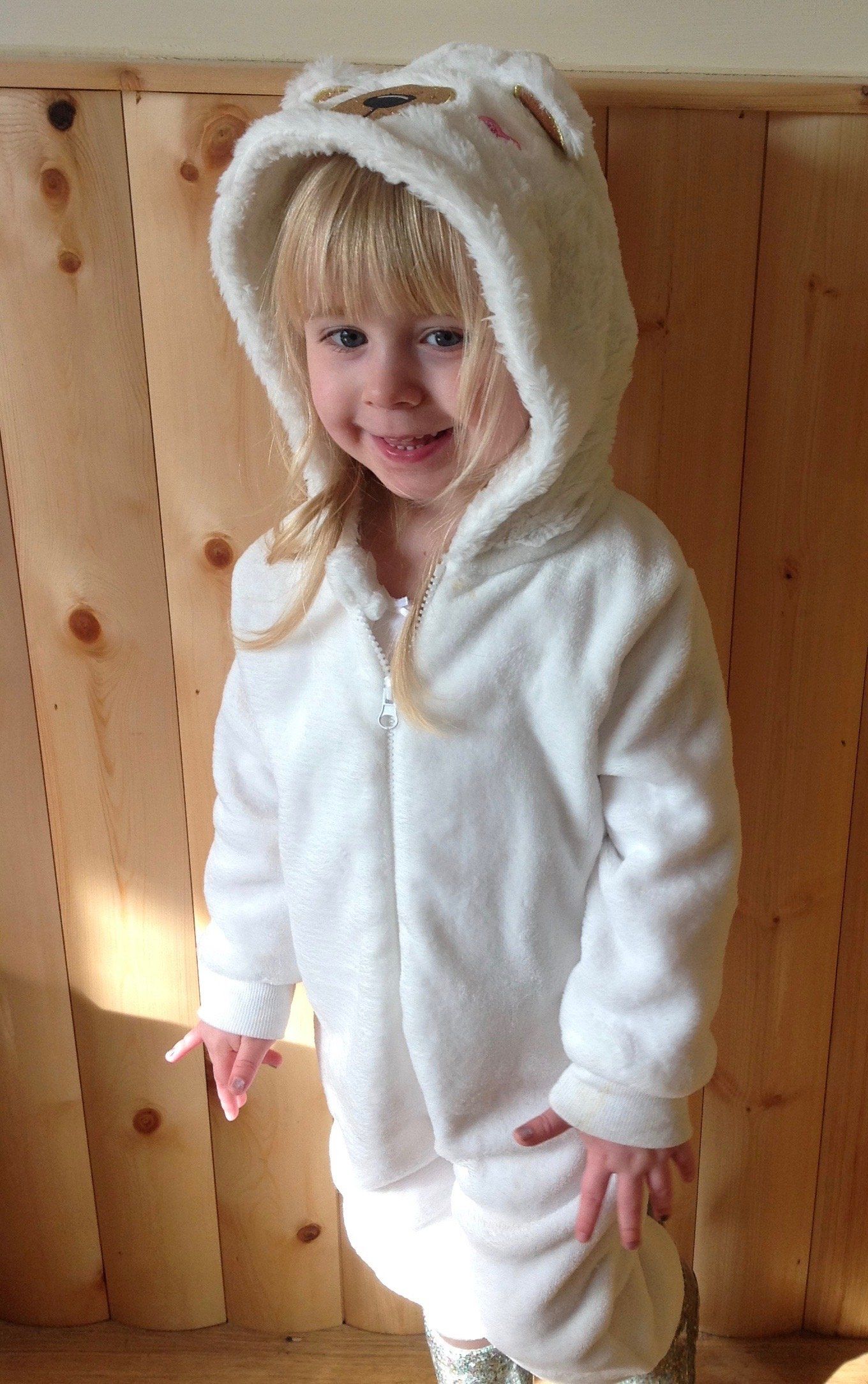 Child in a fluffy white hooded outfit with animal ears, standing indoors and smiling.