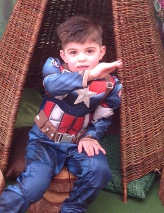 Child in a Captain America costume posing with arms crossed on a wicker chair