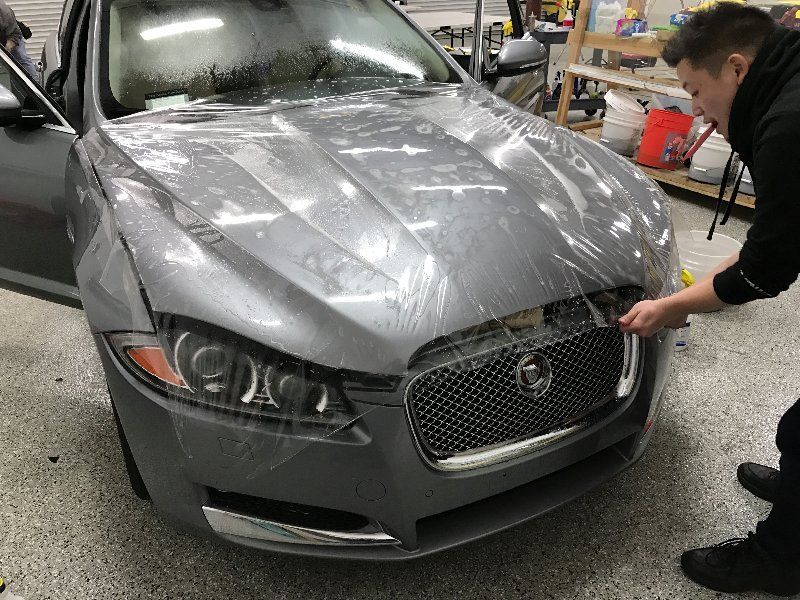 A man is covering a jaguar car with plastic wrap.